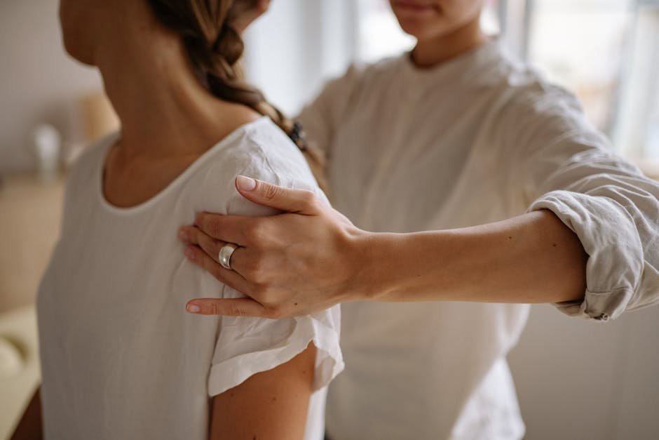 A detailed view of a physiotherapy session with hand placement on shoulder indoors.