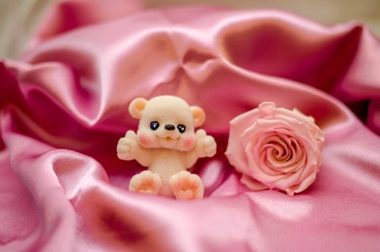 Adorable plush bear toy with a pink rose resting on luxurious pink satin fabric. Ideal for themes of love and romance.