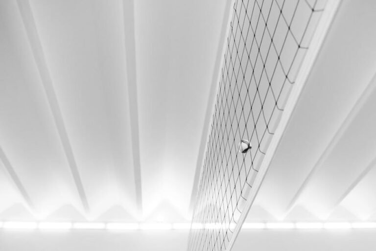 A modern minimalist shot of a volleyball and net indoors, emphasizing geometric patterns and soft lighting.
