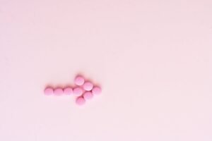 Flat lay of pink pills forming an arrow on a soft pink surface.