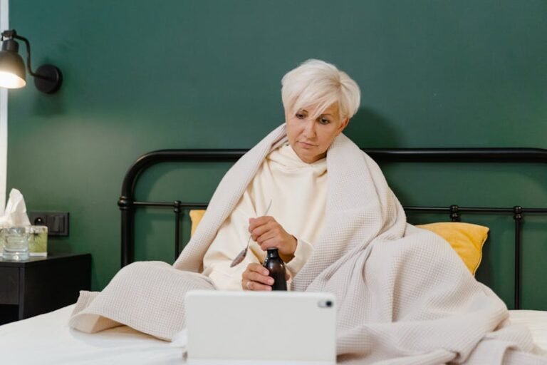 Senior woman wrapped in blanket using tablet for online medical consultation, indoors.