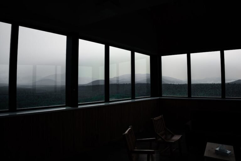 A tranquil landscape view of mountains through large windows in a dark room.