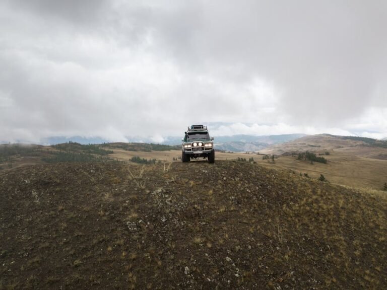 Old SUV car parked on top of hill in mountainous terrain on cloudy day