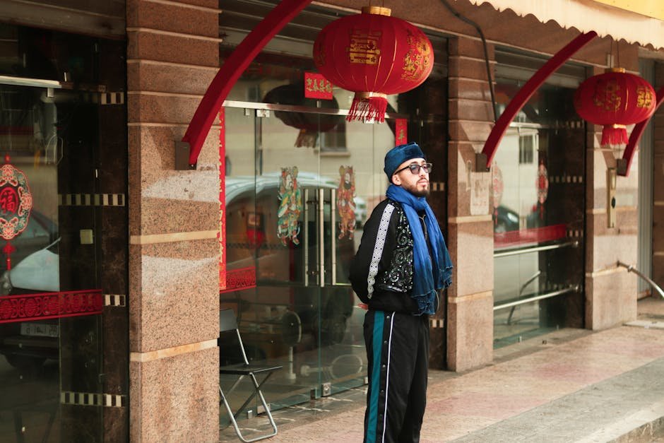 Man in blue scarf and glasses, standing by red lantern decorations outdoors.