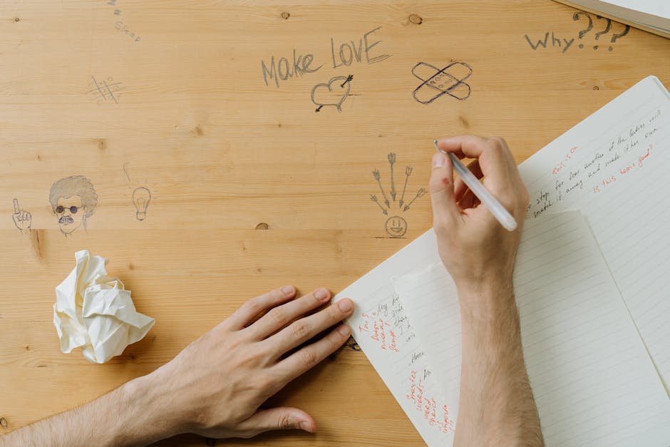 A person drawing on a wooden desk covered in creative doodles and handwritten notes.