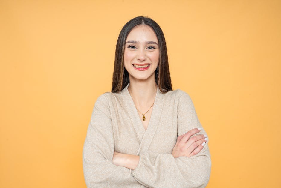 A confident young woman smiling with braces, standing against a vibrant orange background.